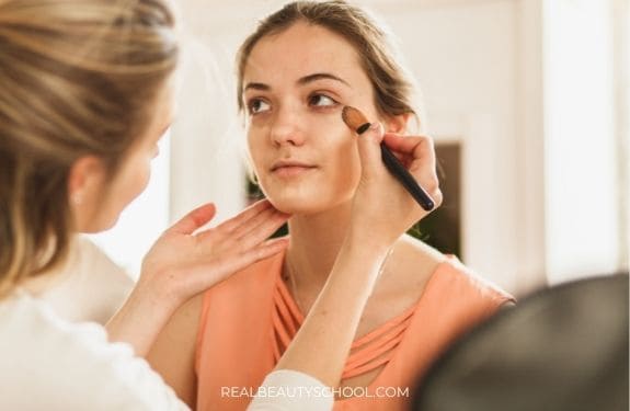 woman applying concealer and foundation to a makeup client